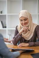 un profesional y confidente asiático musulmán mujer de negocios que se discute trabajo con su colega en el oficina. foto