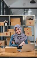 Muslim asian woman freelancer  entrepreneur, Smile for sales success after checking order from online shopping store in a laptop at home office, Concept of merchant business online and eCommerce photo