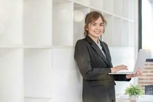 Young businesswoman standing and holding laptop working at office photo