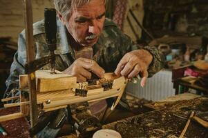 Craftsman in workshop making wooden toy, a wooden model of sailboat. Carpenter sticks a wooden part on a wooden ship photo