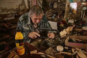 un maduro madera artesano sierras un pedazo de madera sujetado en un vicio con un sierra. artesano haciendo hecho a mano arte de madera juguetes carpintero en acción foto