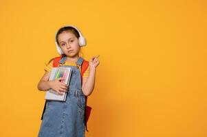 inteligente primero grado estudiante niña en auriculares y casual mezclilla mono, puntos aparte un Copiar publicidad espacio para texto foto