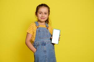 Smiling kid girl holds a smart mobile phone with white blank mockup digital touch screen. Copy ad space for mobile app photo