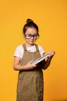 Vertical studio portrait of confident serious little kid girl 6 years old, holding textbook, isolated orange background photo