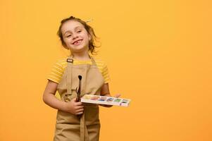 Happy talented inspired little painter girl 6 years old, primary school student with painting tools, smiles at camera photo