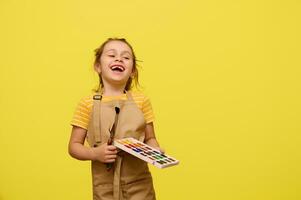 dañoso contento pequeño niño niña risas, expresa contento positivo emociones durante Arte clase, aislado amarillo antecedentes foto