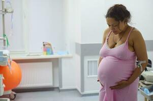 embarazada mujer parto madre con doloroso contracción, conmovedor barriga y mirando abajo. parto proceso a hospital foto