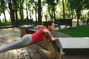 Determined Hispanic woman enjoying morning functional cross workout in city park on a beautiful hot sunny summer day photo