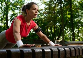 Motivated Hispanic female athlete, muscular build woman in bright sportswear performing push ups from during functional cross training in forest park photo