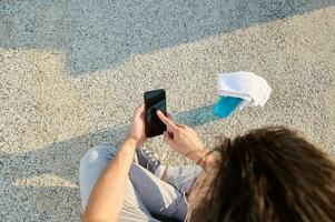 gastos generales ver F un deportista sentado en el pavimento y hojeada el aplicación en su teléfono inteligente parte superior ver de un atleta comprobación móvil teléfono. Copiar espacio foto