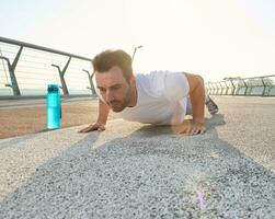 medio Envejecido europeo deportista, atleta, atleta ejecutando hacer subir ejercicio durante al aire libre rutina de ejercicio en el vaso ciudad puente a amanecer. deporte, gimnasia, activo y sano estilo de vida foto