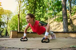 Push beyond your limits. Sportswoman doing push ups during functional full body workout in urban landscape park photo