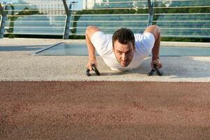 Front view of a determined sportsman doing push-ups , pumping chest and shoulders muscles during morning workout outdoor. Keep your body fit and enjoy summer moments photo