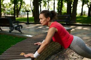 Middle-aged active African American woman doing pushups on the city park photo
