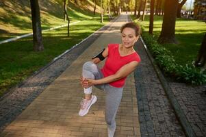 Determined cheerful African American fit woman in gray leggins and red tight t-shirt exercising outdoor in the city park. Fitness, body weight training outdoor on a warm summer day photo
