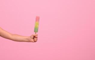 Healthy vegan ice cream popsicle in hand of a baby girl isolated on pink wall background with copy space . Summer dessert and cheerful summer mood concept photo