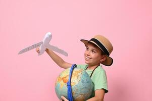 Adorable child boy plays with a paper airplane simulating a flight around the planet Earth. Concepts about travel, tourism, geography and aviation. Pink background with copy space photo