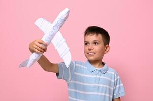 Handsome schoolboy playing with a paper airplane against pink background with copy space. Tourism, travel, geography knowledge concepts photo