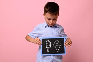 A boy looking at a chalkboard in his hand with drawn ice cream against pink background with copy space. concepts photo