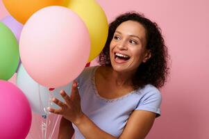 Beautiful gorgeous attractive stunning cheerful woman cute smiling with beautiful toothy smile peeking through inflated bright air balloons posing against pink colored background with space for text photo