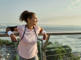 Middle aged female athlete with a jumping rope, standing on the modern glass city bridge, enjoying early sunny morning cardio workout outdoor. Cardio workout concept photo