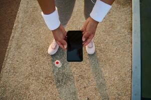 Top view of female athlete hands in white terry wristbands holding a smartphone with empty blank black screen and browsing on websites and mobile applications. photo