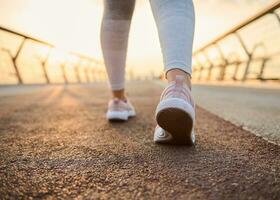 Close-up female athlete feet in pink sneakers on a treadmill at sunrise background. Cropped image of the legs of a sportswoman running jogging on a city bridge with sun beams falling on treadmill photo