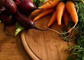 Bunches of fresh organic beets and baby carrots with tops on a wooden cutting board. Vegan food background. photo