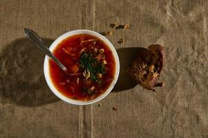 Overhead view of the borscht, Ukrainian traditional soup with healthy vegetables and tomatoes, whole grain bread and crumbs on a linen tablecloth photo