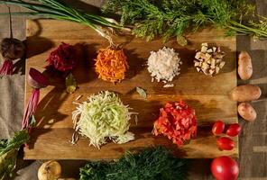 Grated raw vegetables -beet, carrot onions, tomatoes, potatoes, cabbage and fresh green wet dill on a wooden cutting board. Flat lay of chopped ingredients for a traditional Ukrainian soup- borscht. photo