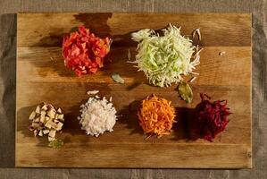 Flat lay of chopped ingredients for a traditional Ukrainian soup- borscht. Chopped and grated raw fresh vegetables -beet, carrot onions, tomatoes, potatoes, and cabbage on a wooden cutting board. photo