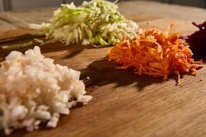 Chopped and grated raw fresh vegetables -beet, carrot onions and cabbage on a wooden cutting board. Close-up of chopped ingredients for a traditional Ukrainian soup- borscht photo