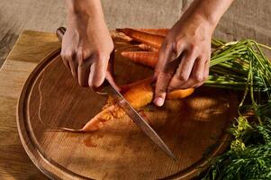 parte superior ver de hembra manos corte, el cortar, rebanar Fresco crudo bebé Zanahoria en un de madera tablero. de cerca de mano con cuchillo corte Fresco vegetal. foto