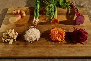 Close-up of seasonal fresh raw vegetables on a wooden board, cut in half and the other half shredded on a grater. Beets, carrots, green onions with leaves and potatoes. Food background photo