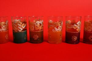 Multicolored glasses for Moroccan green mint tea, decorated in oriental style. Isolated on red background photo