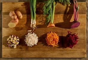 Top view of seasonal fresh raw vegetables on a wooden board, cut in half and the other half shredded on a grater. Beets, carrots, green onions with green leaves and potatoes photo