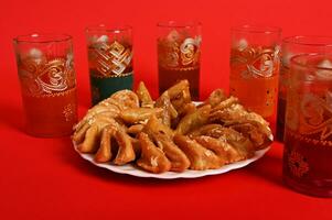 Multicolored glasses of mint tea in Moroccan tradition, with beautiful decoration and a plate with Arabic sweet dessert in the foreground. Isolated on red background with copy space photo