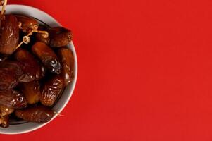 Cropped image of a plate full of fresh mediterranean delicious and tasty dates. Red background, copy space photo