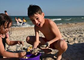 Little children playing at the sandy beach. Adorable kids building sandy castles. Focus on handsome funny boy enjoying summer holidays at the island photo