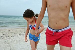 Soft focus on a beautiful girl in a swimsuit holding her older brother by the hand. Friends walking along the beach. Children enjoy summer vacation at the sea, in the open fresh clean air photo