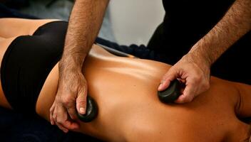 Ayurvedic hot stone massage in modern spa salon. Bodycare concept. Masseur massaging woman's back with lava stones photo