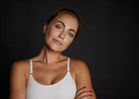 Close-up beauty portrait of a beautiful attractive charming middle aged European woman in white top smiles looking at camera isolated over black background with copy ad space photo