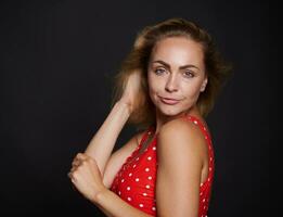 Beautiful middle aged blonde sporty European woman in red swimsuit with white polka dots confidently looking at camera isolated over black background with copy ad space photo