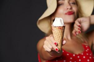 suave atención en hielo crema en el manos de un alegre sexy rubia mujer en rojo traje de baño con blanco polca puntos y un verano sombrero, aislado terminado negro antecedentes con Copiar anuncio espacio. verano Días festivos concepto foto