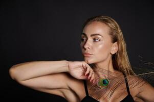 Close-up attractive middle aged blonde Caucasian woman with healthy fresh clean skin and wet blond hair holding a peacock feather, isolated over black background with copy ad space photo