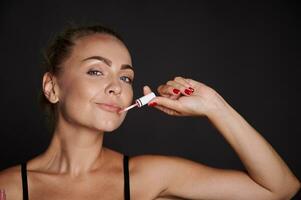 Natural beauty Caucasian middle aged woman applying moisturizing shining lip gloss. Make-up concept photo