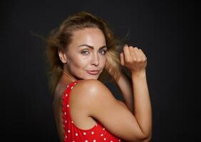 retrato de un atractivo europeo mujer con natural maquillaje y sano brillante bronceado piel, brillante volador rubio cabello, vistiendo rojo traje de baño aislado terminado negro antecedentes con Copiar espacio para anuncios foto