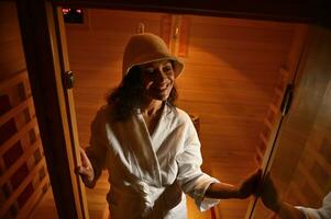 Smiling African American ethnicity woman in infrared wooden sauna. Spa treatment. Body and skin care photo