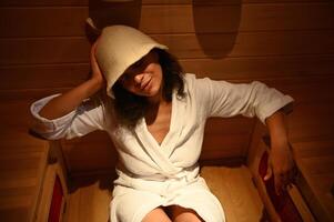 Close-up of beautiful woman with eyes closed enjoying spa procedure in infrared sauna photo