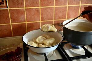 The pastry chef takes out cooked dumplings from boiling water into a colander photo